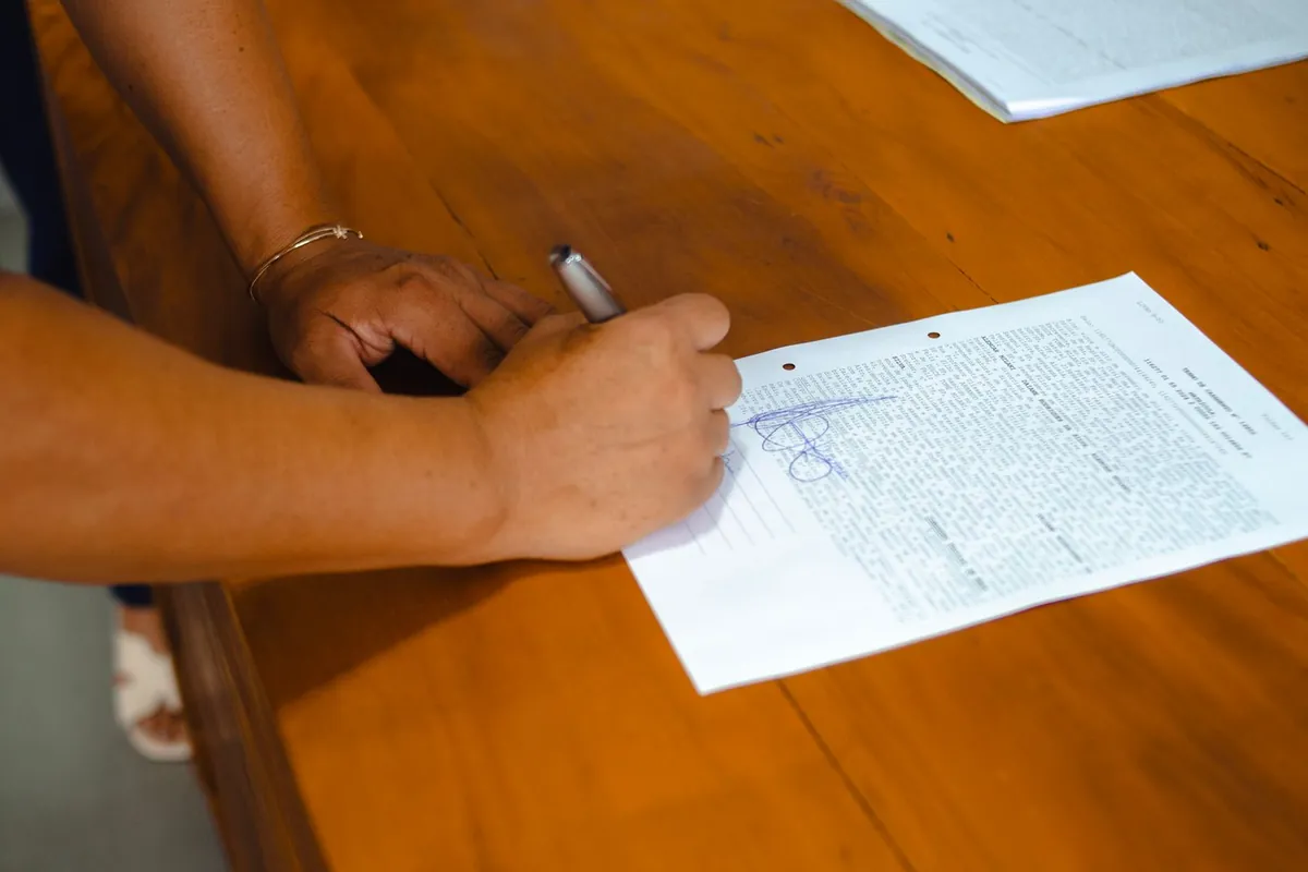 Una mano firma un documento sobre una mesa de madera.